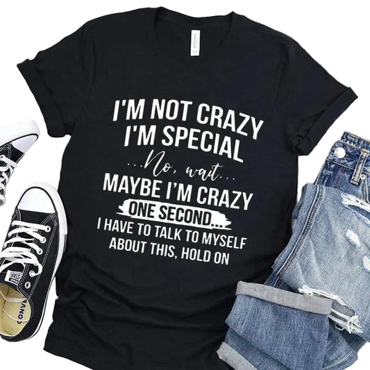 Black t-shirt with humorous text design on a wooden surface with shoes and jeans.